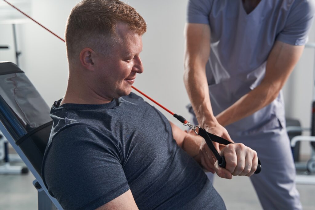 Physician helps man with disability lift weight with hand on simulator