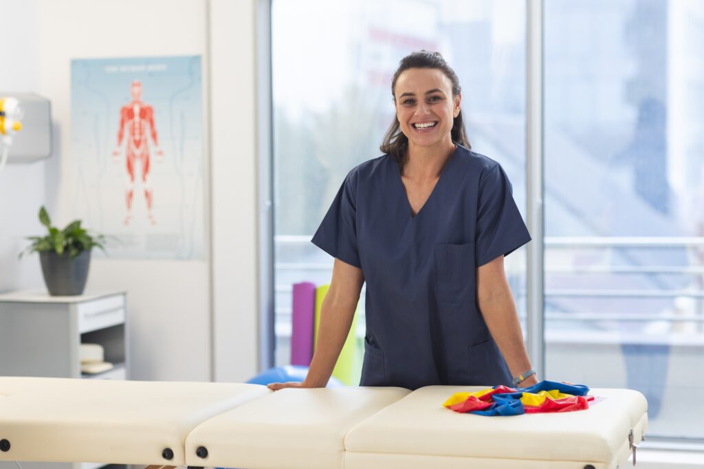 Portrait of happy female caucasian physiotherapist wearing scrubs at hospital