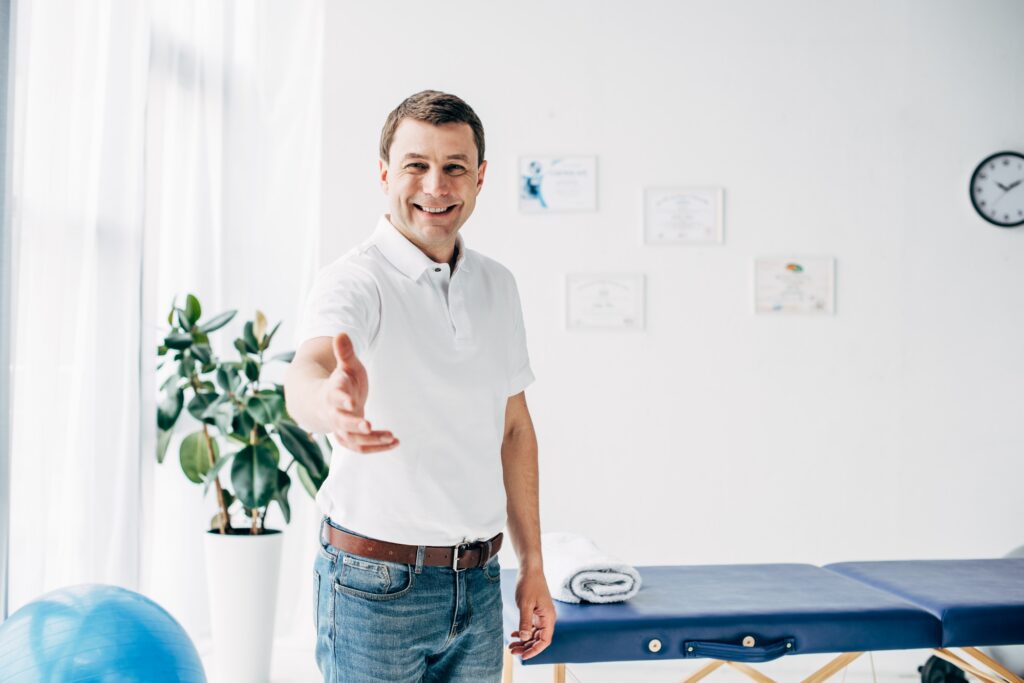 smiling chiropractor with outstretched hand looking at camera in massage cabinet